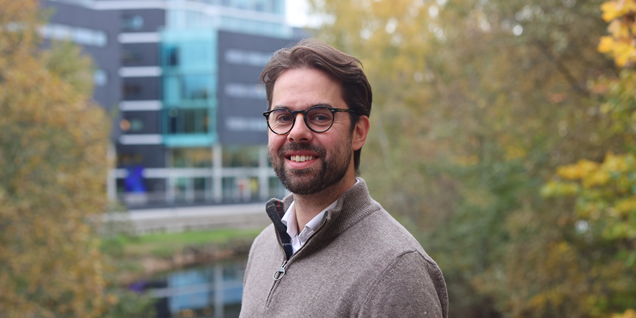 Man with glasses smiling in front of an office building